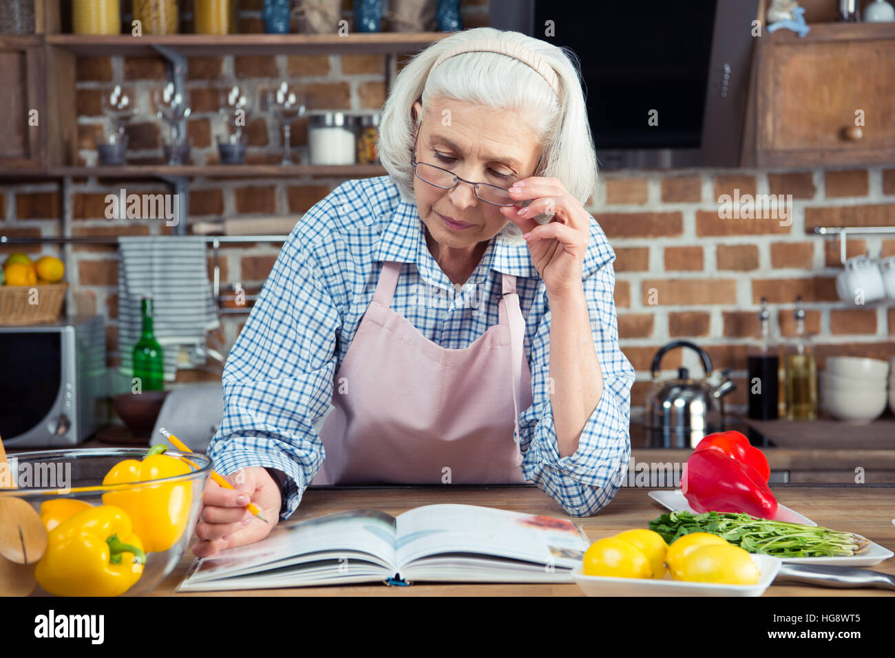 Grave donna senior cercando nel libro di cucina durante la seduta in cucina Foto Stock