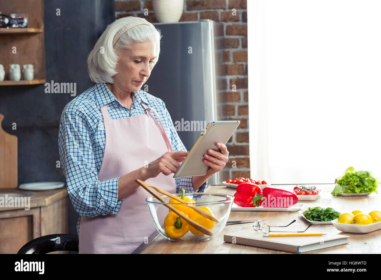 Donna senior con tavoletta digitale in cucina durante la preparazione di insalata di verdure Foto Stock