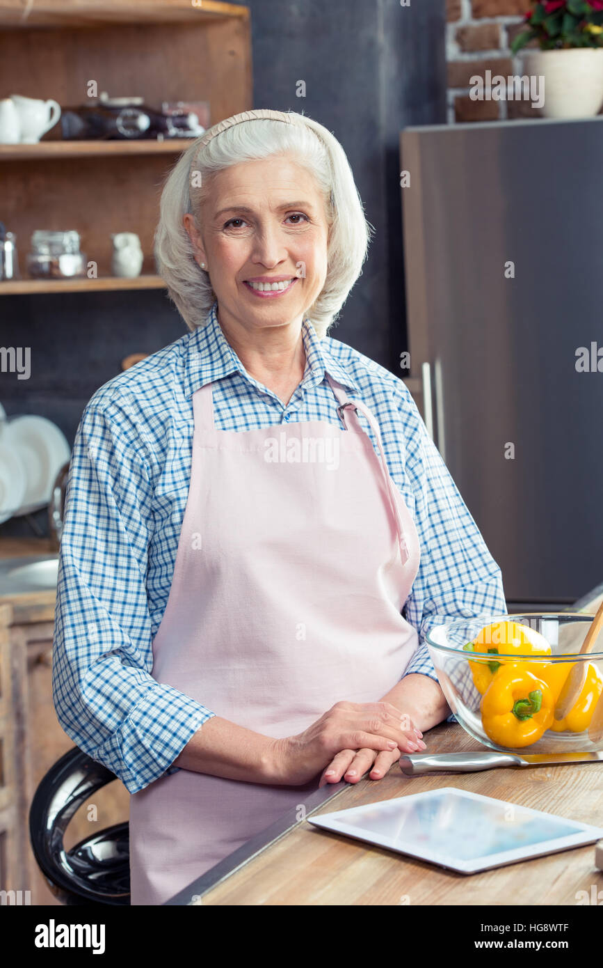 Senior donna in grembiule sorridente in telecamera in cucina Foto Stock