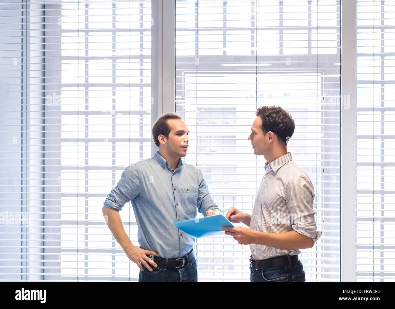 Due colleghi parlare insieme sui documenti di progetto in piedi nel moderno e luminoso interno di office Foto Stock
