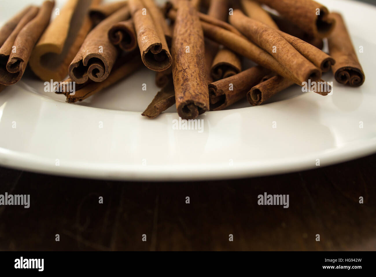 Un mucchio di bastoncini di cannella su una piastra bianca, fotografato vicino a un tavolo di legno. Foto Stock