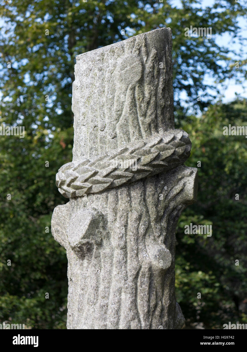 Una singola lastra tombale scolpita come un taglio tronco di albero vincolato da una corona contro il fogliame verde Foto Stock