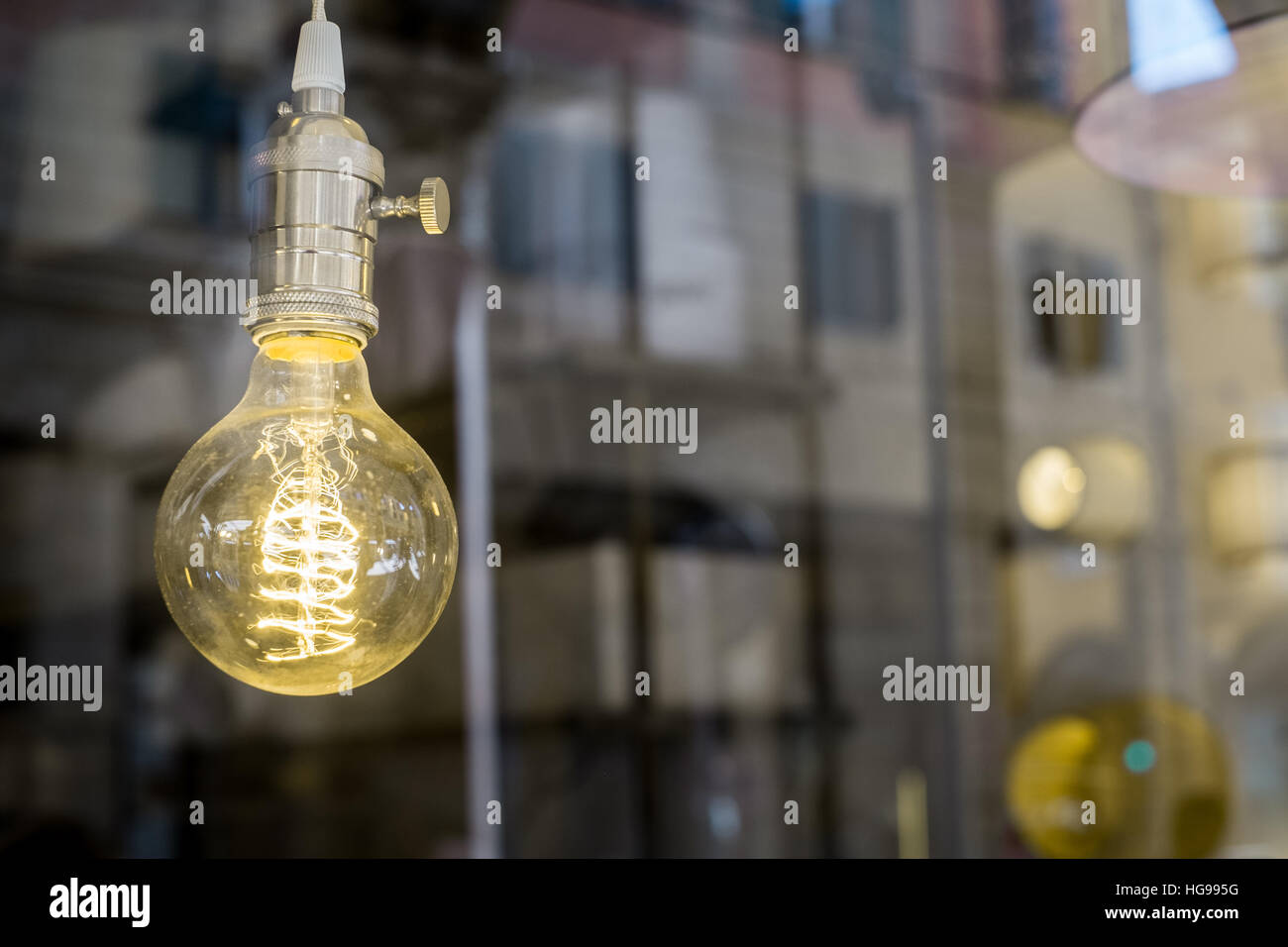 Decorativo Edison vecchio stile lampadina luce contro sfocata scena urbana sfondo riflettente Foto Stock