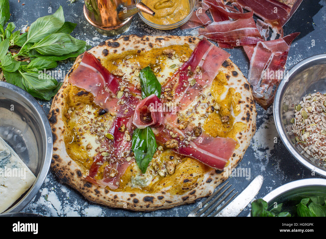 Tradizionale pizza italiana con pesto di zucca, prosciutto, gorgonzola e semi sulla lavagna Foto Stock