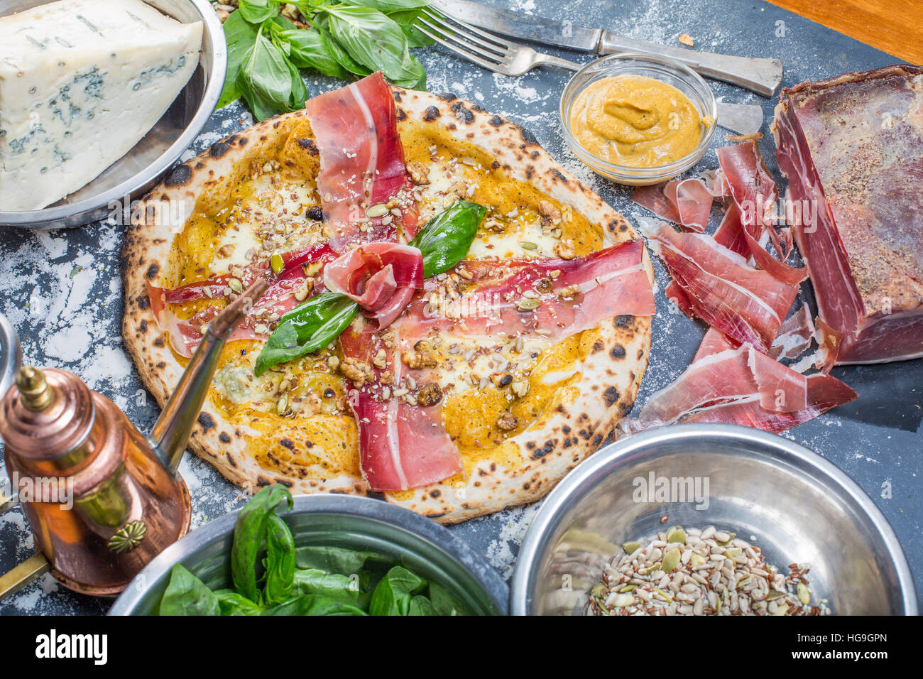 Tradizionale pizza italiana con pesto di zucca, prosciutto, gorgonzola e semi sulla lavagna Foto Stock