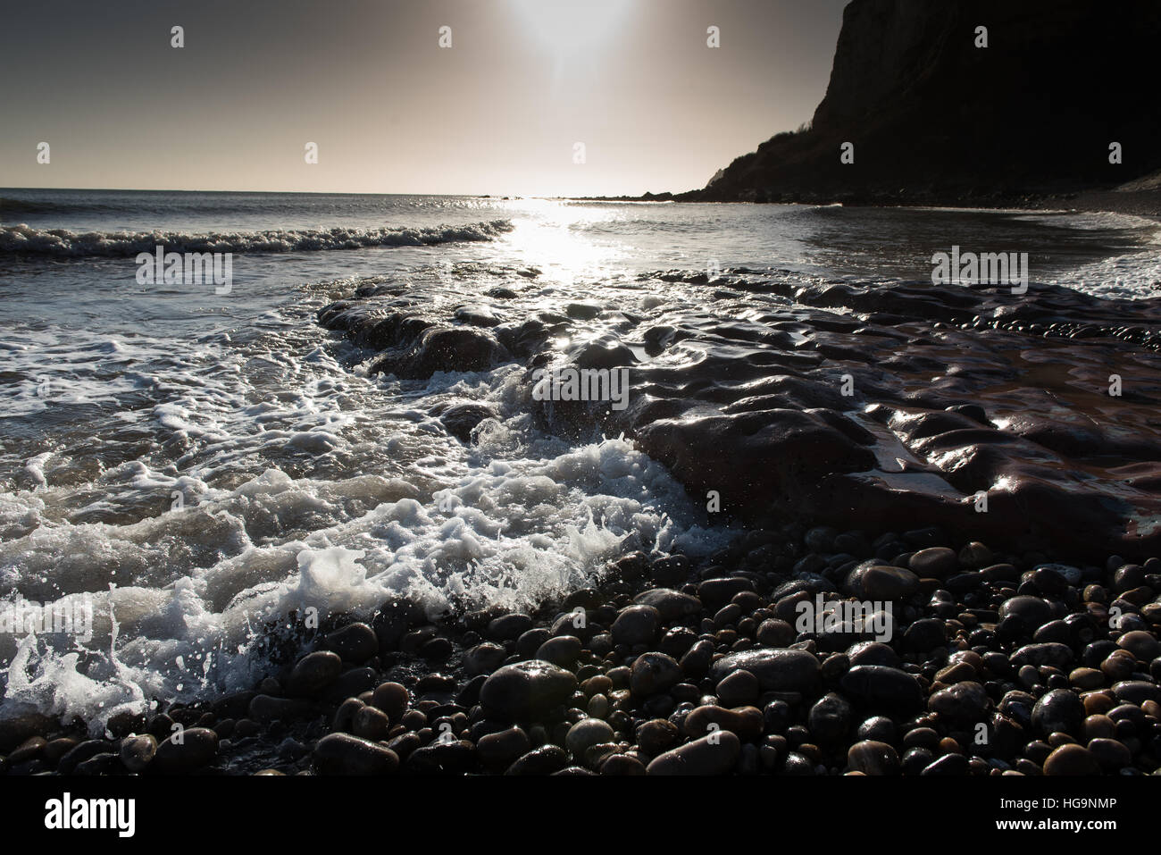 La bassa inverno il sole brilla sulle onde & wet ciottoli della East Devon spiaggia di Seaton. Foto Stock