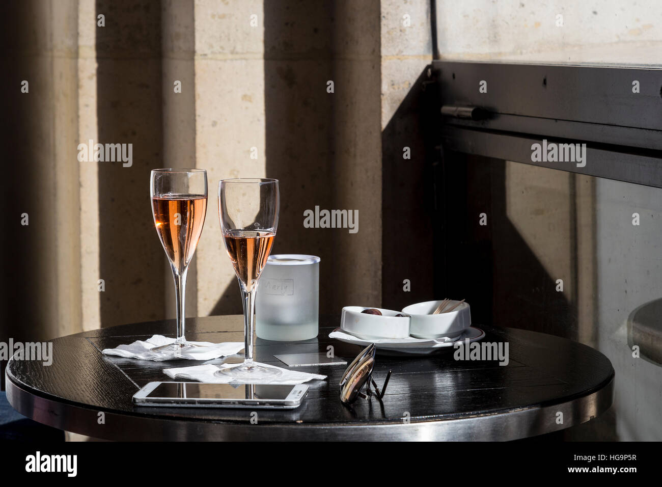 Due bicchieri di vino rosato, telefono cellulare, occhiali da sole e una tazza di olive in Le Café Marly, Parigi, Francia Foto Stock