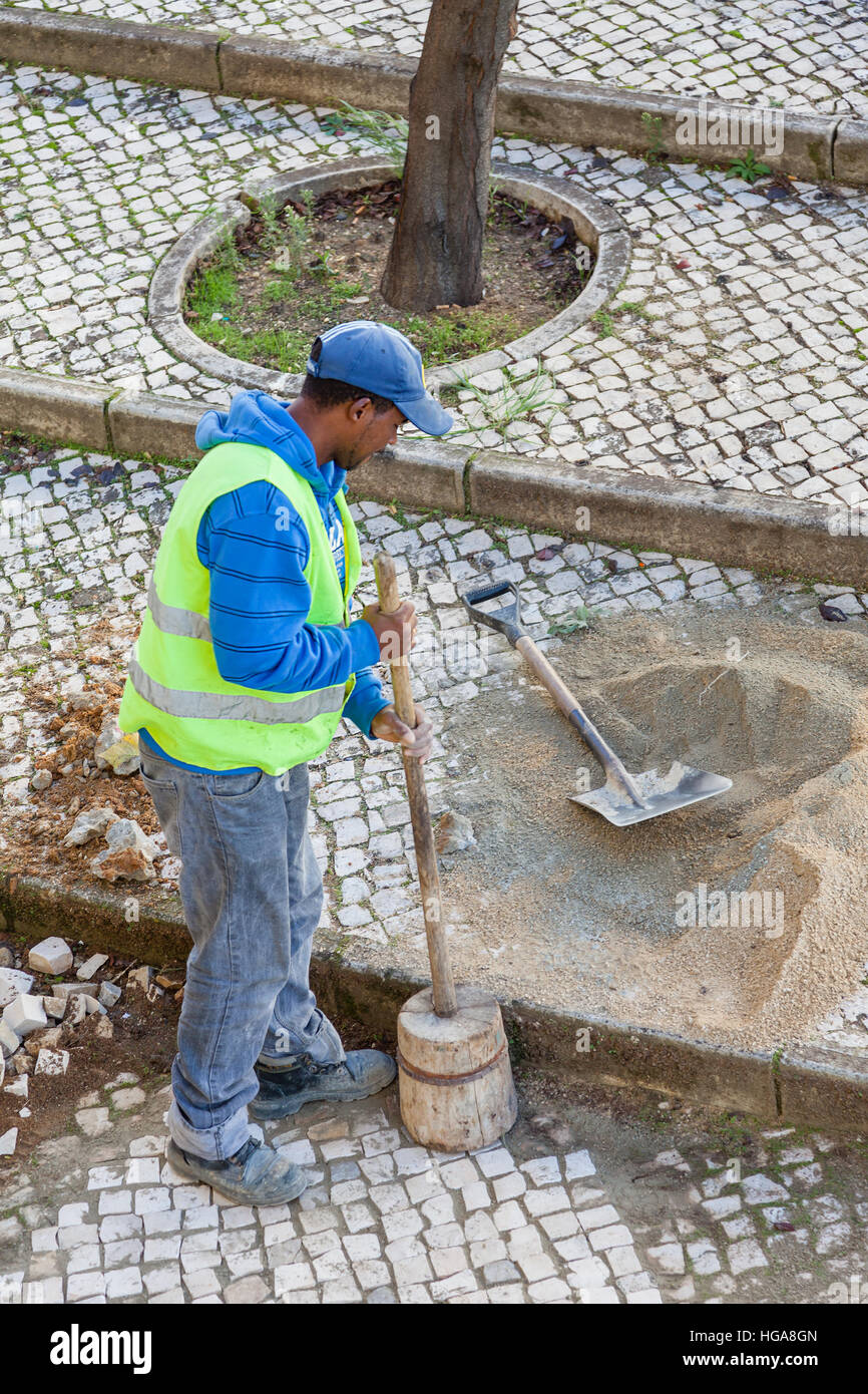 Lavoratore a riparare il marciapiede marciapiede con il tradizionale a mano acciottolato. Comprimendo i ciottoli colpendole. Foto Stock