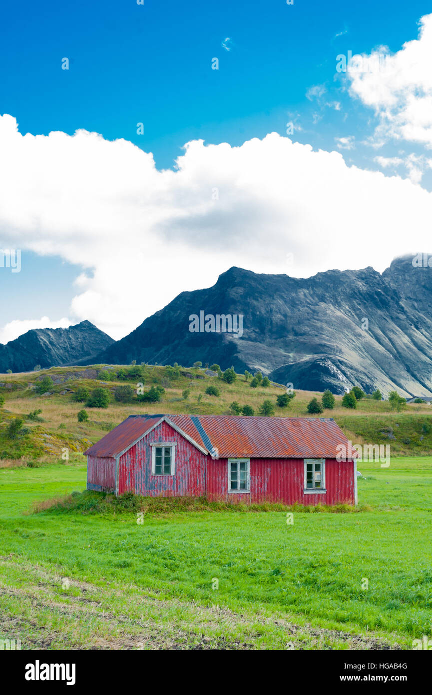 Piccoli abbandonati in legno rosso casa in campagna con i verdi campi e montagne sullo sfondo Foto Stock