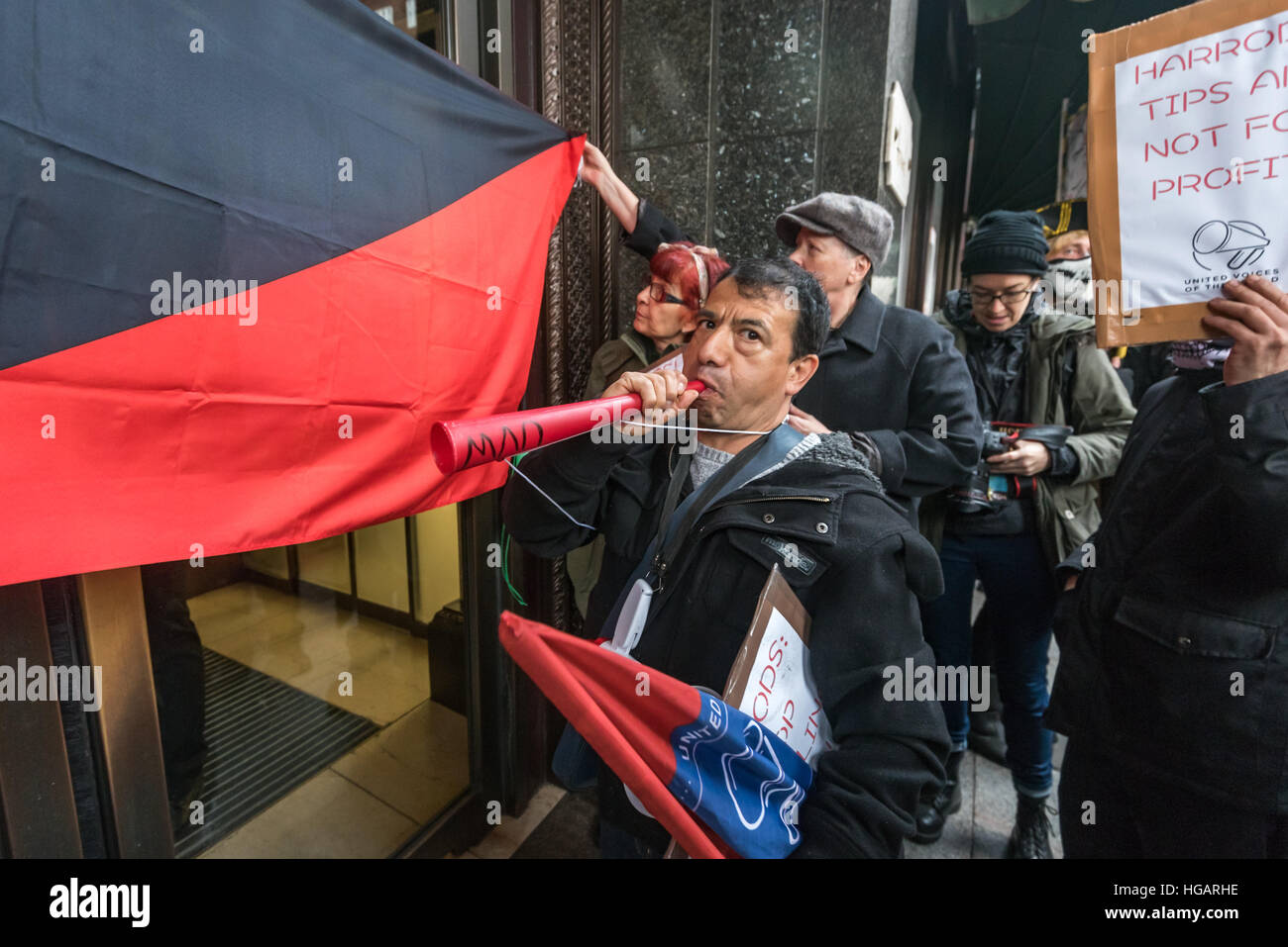 Londra, Regno Unito. Il 7 gennaio 2017. Manifestanti tenere premuto su un anarchico bandiera attraverso la porta o Harrods per interrompere la polizia all'interno di filmare la protesta da parte di radici di erba sindacato United voci del mondo chiamando per il 100% delle spese di servizio per andare al personale piuttosto che la stragrande dei profitti dei proprietari, Qatar famiglia reale. Credito: Peter Marshall / Alamy Live News Foto Stock