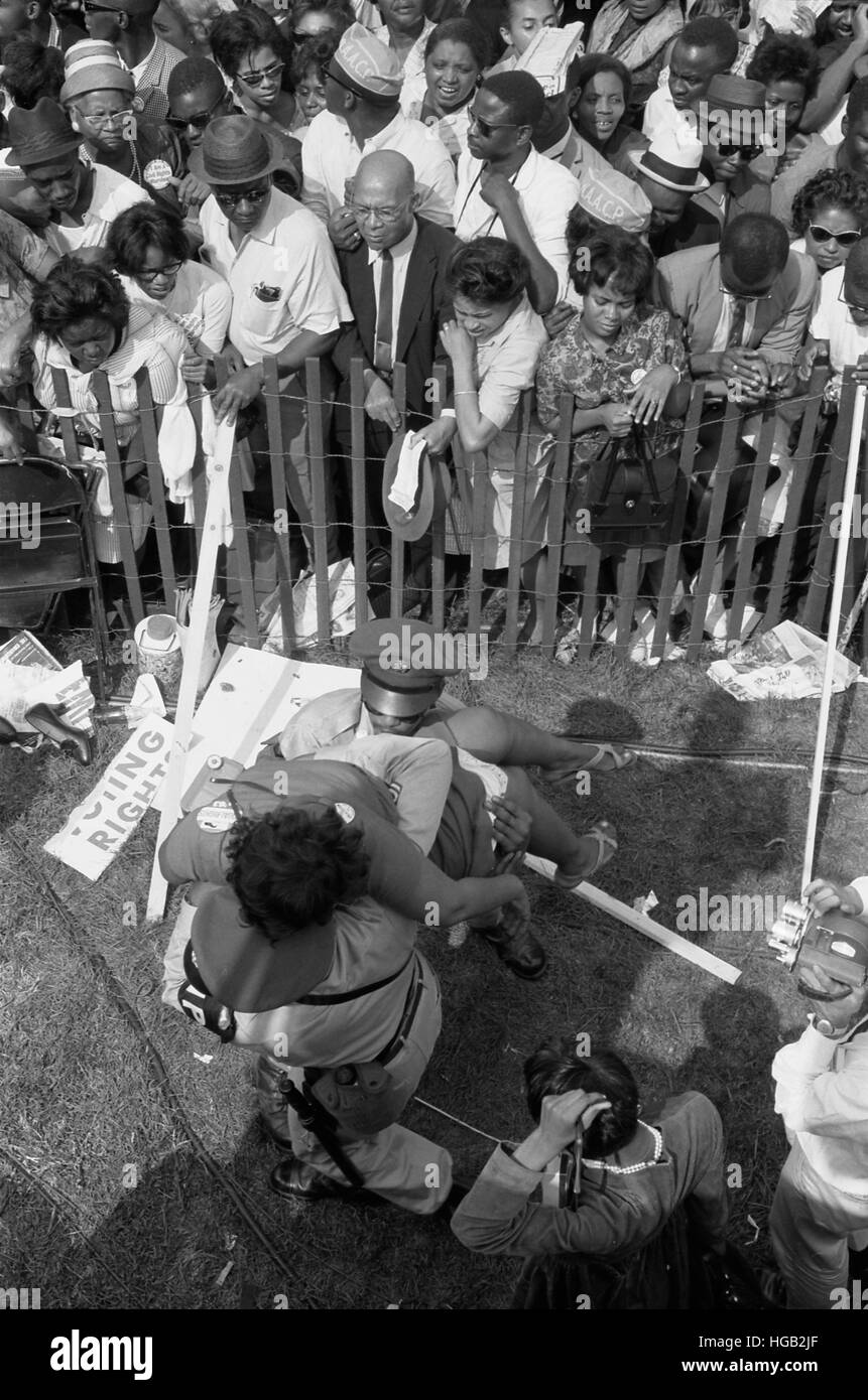 Una folla di americani Africani dietro un recinto con la polizia che porta una donna su altro lato, 1963. Foto Stock