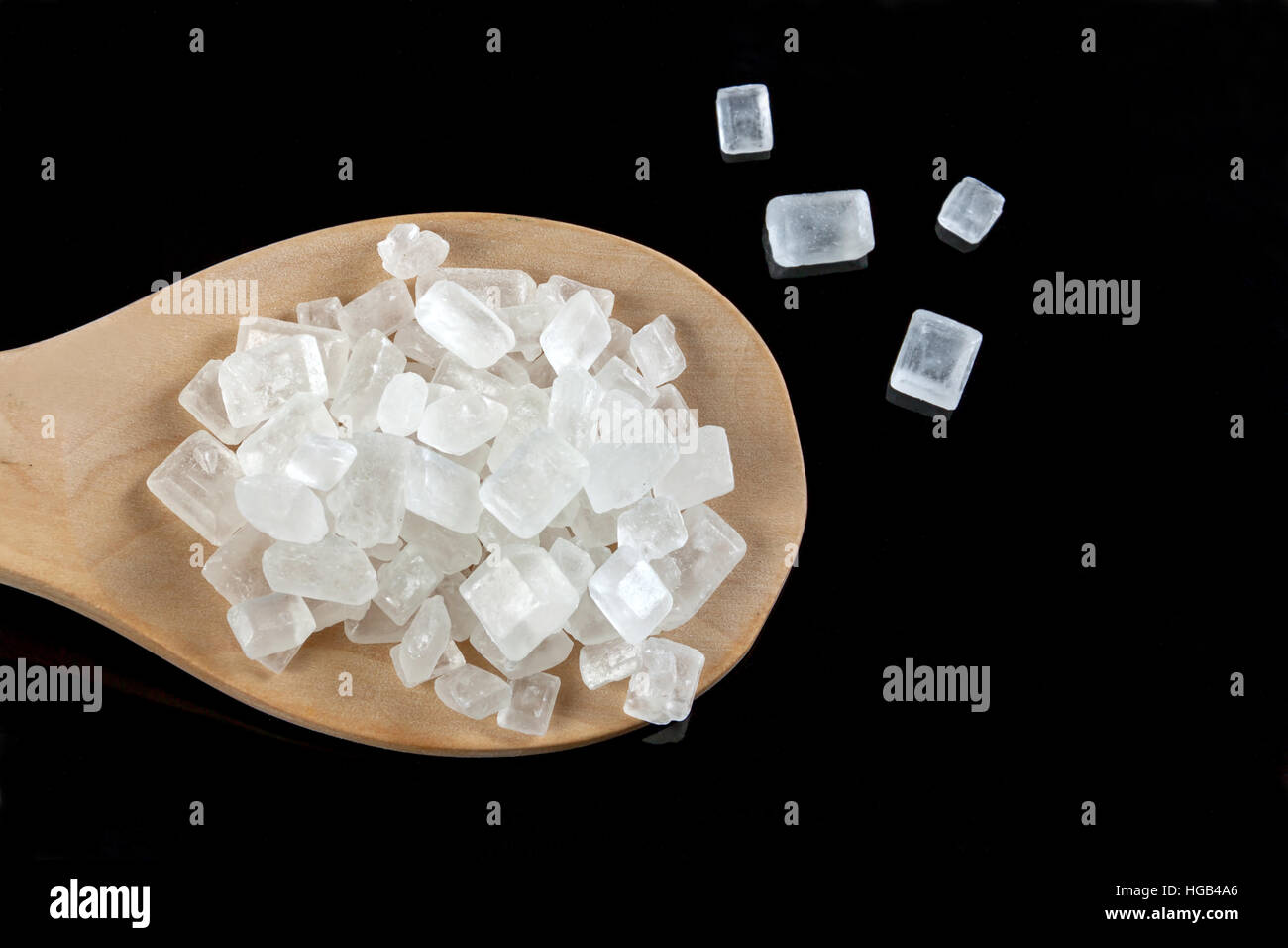 Rock lo zucchero bianco in un cucchiaio di legno su sfondo nero. Pura dello zucchero di canna per il naturale. senza additivi. Foto Stock