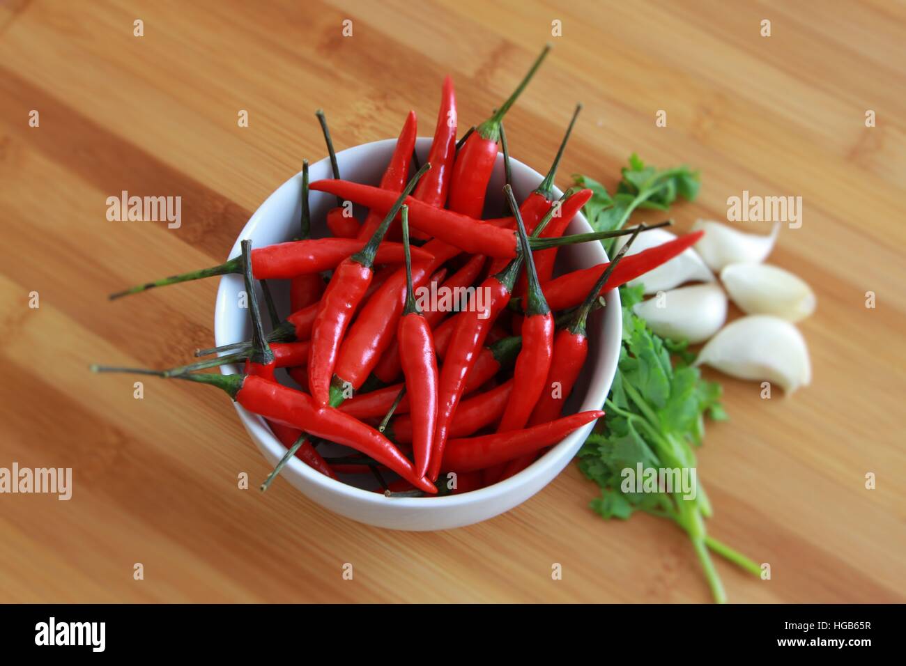 Chili in bianco ciotola con il coriandolo e aglio su sfondo di bambù Foto Stock