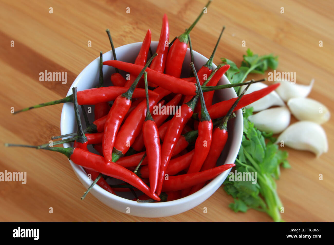 Chili in bianco ciotola con il coriandolo e aglio su sfondo di bambù Foto Stock
