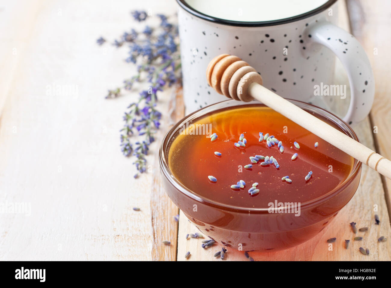 Vaso di vetro con miele e lavanda, tazza di latte su una luce sullo sfondo di legno Foto Stock