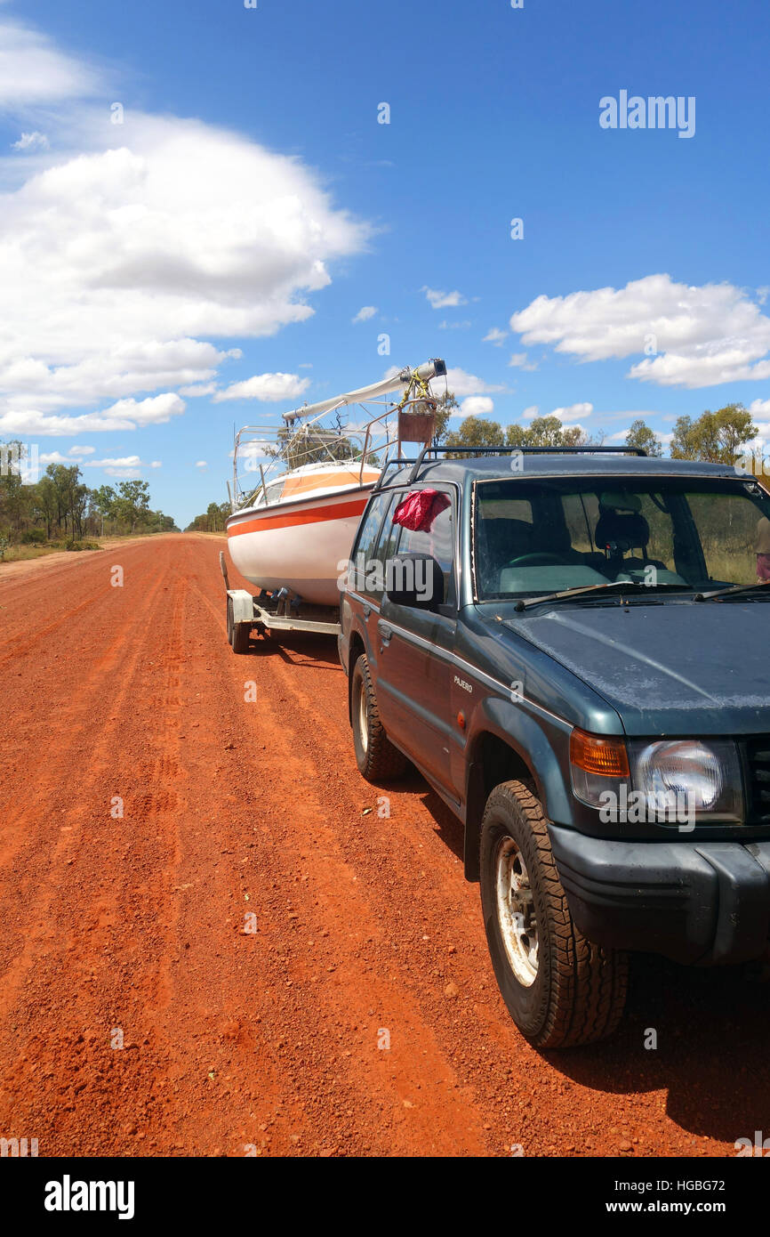 Con quattro ruote motrici auto traino del rimorchio sailer yacht su ondulato rosso su strada sterrata, vicino Barcaldine, Queensland, Australia. N. PR Foto Stock