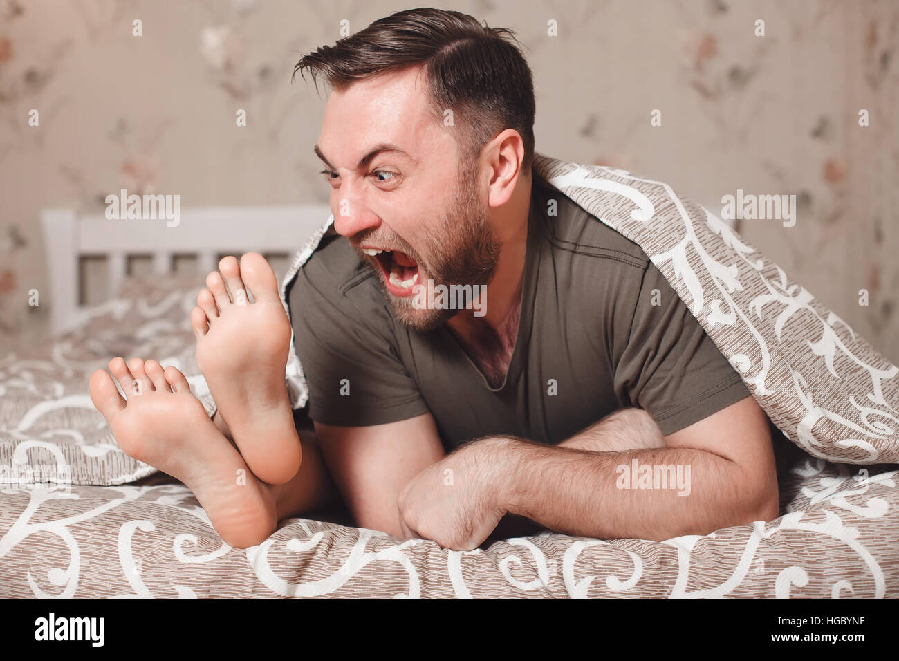 Uomo che cerca di mordere donna di piedi nel letto. Foto Stock
