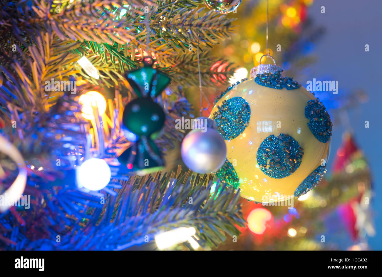 Addobbi per l'albero di Natale. Giallo, finitura brillante orb con i cerchi blu, bagliori, circondato da luminose,vibrante luci multicolori Foto Stock