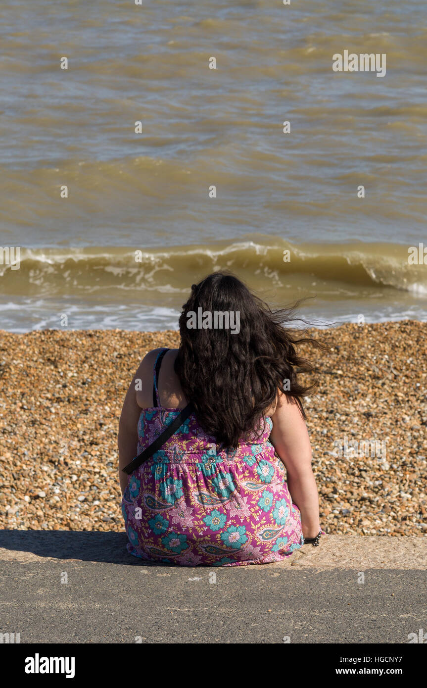 Il sovrappeso o obesi donna seduta da sola, guardando al mare Foto Stock