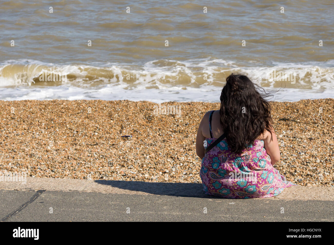 Il sovrappeso o obesi donna seduta da sola, guardando al mare Foto Stock