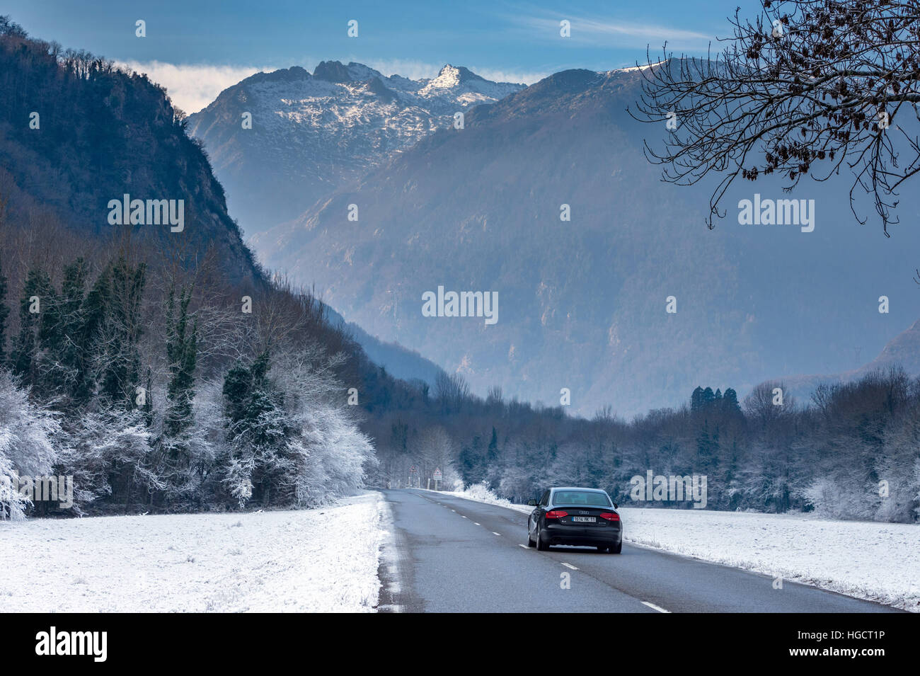 Strada che corre attraverso il paesaggio innevato verso le montagne con auto Foto Stock