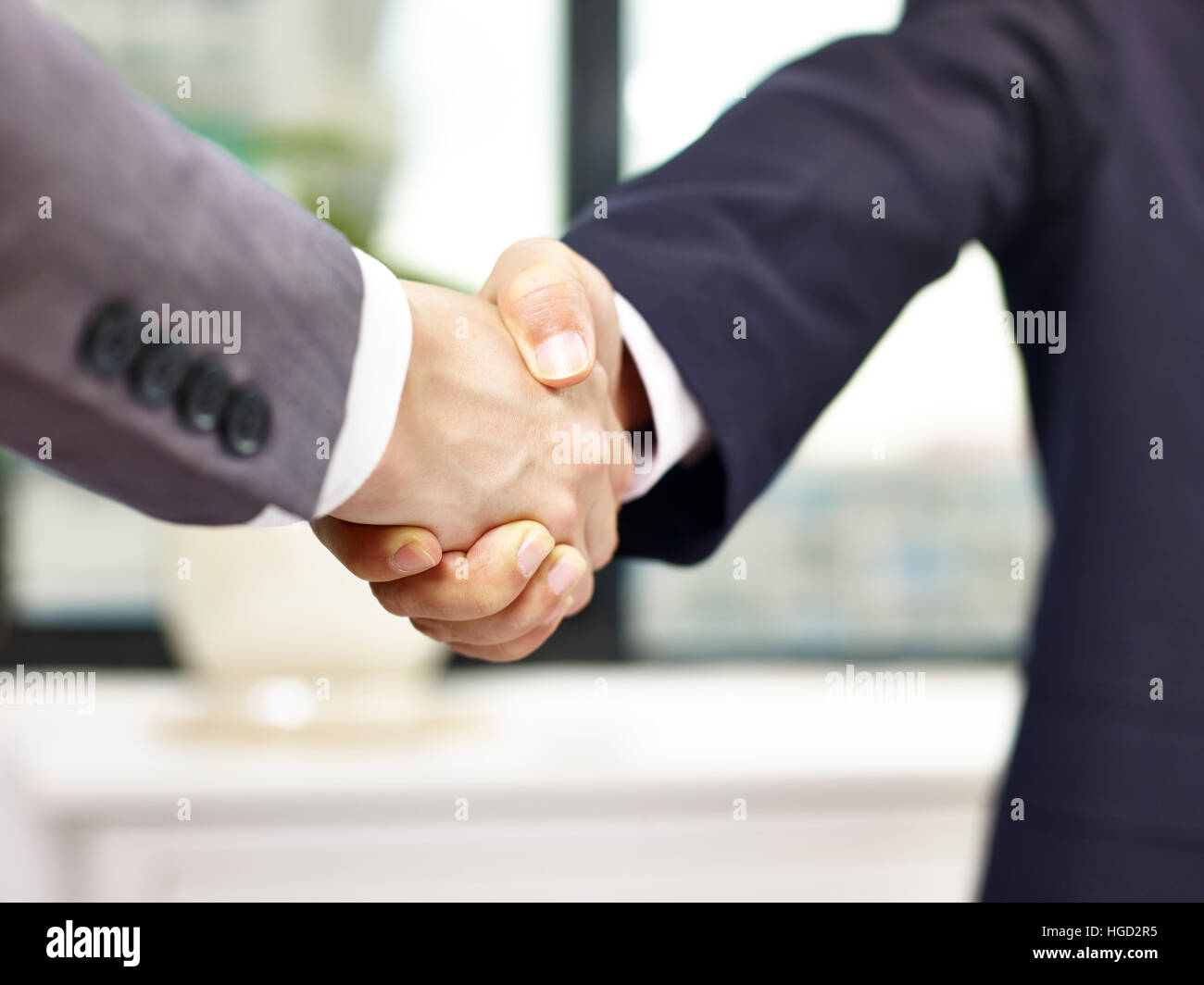Close-up, basso angolo vista di una stretta di mano ferma in ufficio da parte di due imprenditori asiatici. Foto Stock