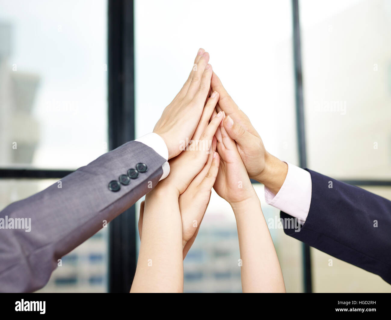 La gente di affari mettendo le mani insieme per formare una piramide di mostrare determinazione o lo spirito del lavoro di squadra. Foto Stock