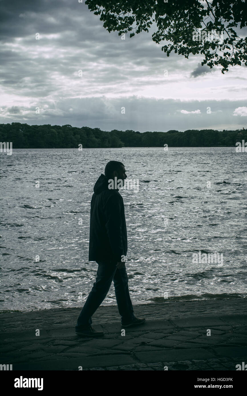 Silhouette di un uomo che cammina in riva al lago Foto Stock