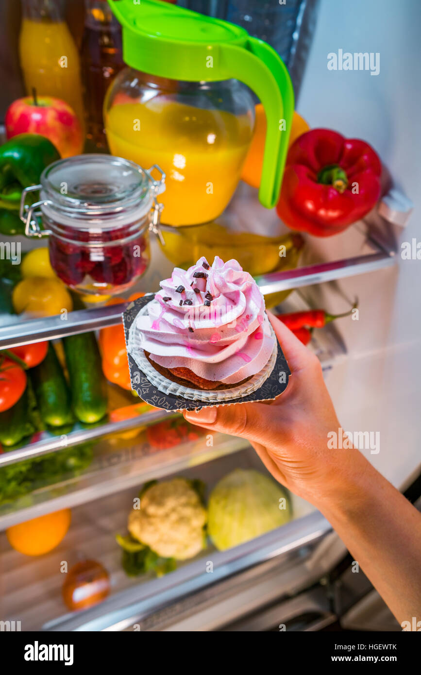 La donna prende la torta dolce dal frigorifero aperto Foto Stock