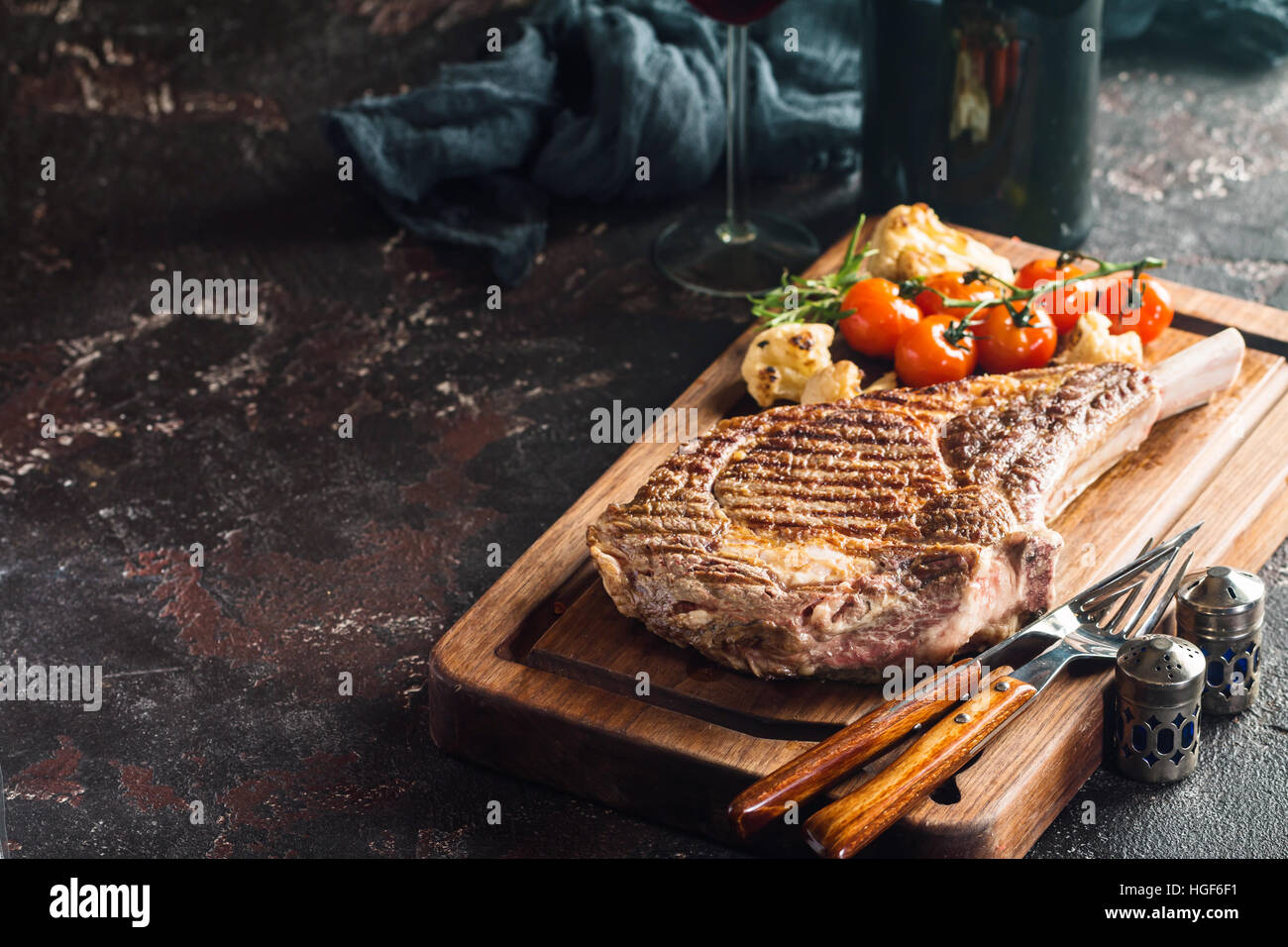 Succulente grigliate di tomahawk bistecca con l'osso con vino rosso, condimenti, di rosmarino fresco e verdure grigliate sul bordo di taglio Foto Stock