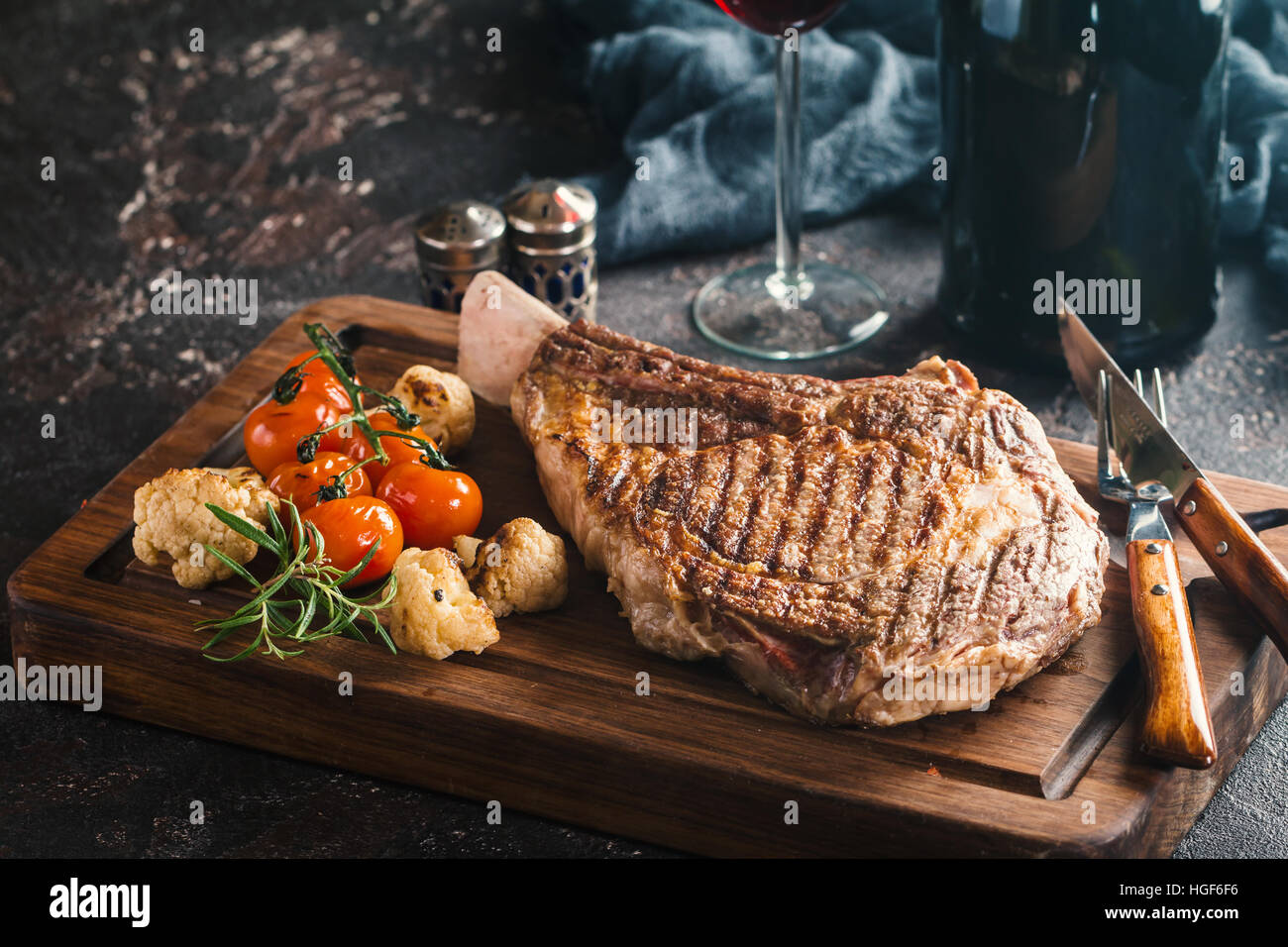Succulente grigliate di tomahawk bistecca con l'osso con vino rosso, condimenti, di rosmarino fresco e verdure grigliate sul bordo di taglio Foto Stock