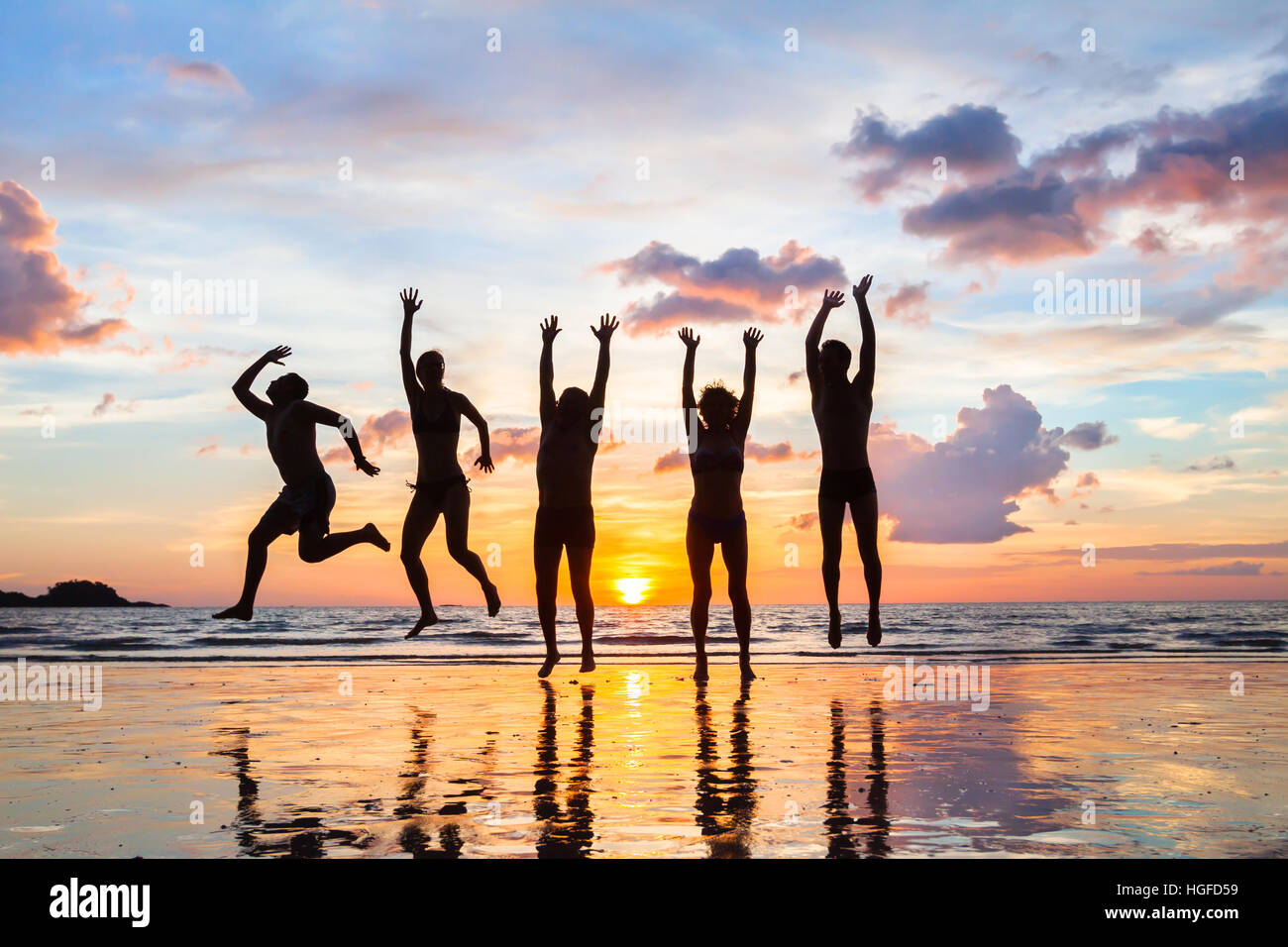 Gruppo di persone che saltano sulla spiaggia al tramonto, sagome di happy amici in vacanza Foto Stock