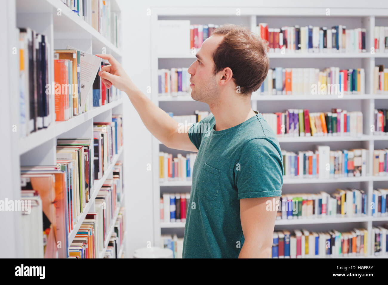 Curioso uomo scegliendo libro in biblioteca o bookshop, studente di letteratura di prelievo dal ripiano Foto Stock