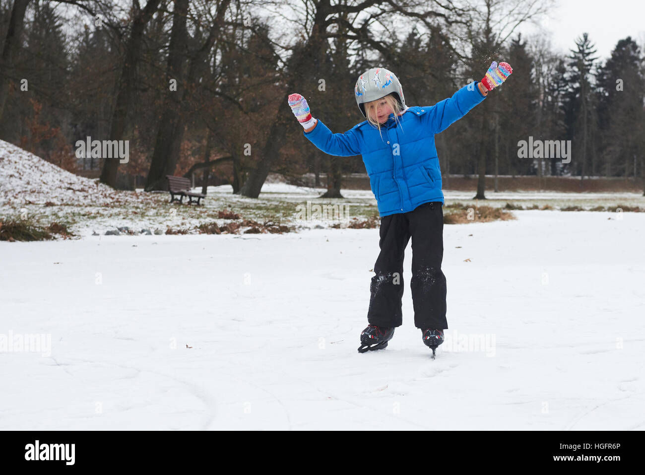 Adorabile bambina ragazza il pattinaggio su ghiaccio in inverno la neve giorno all'aperto nel parco sul laghetto congelato. Indossando il casco di sicurezza Foto Stock