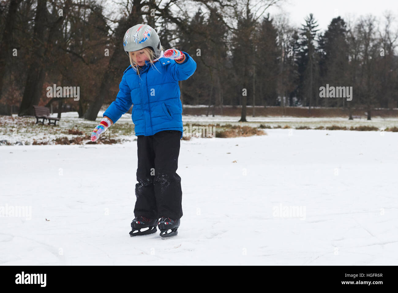 Adorabile bambina ragazza il pattinaggio su ghiaccio in inverno la neve giorno all'aperto nel parco sul laghetto congelato. Indossando il casco di sicurezza Foto Stock