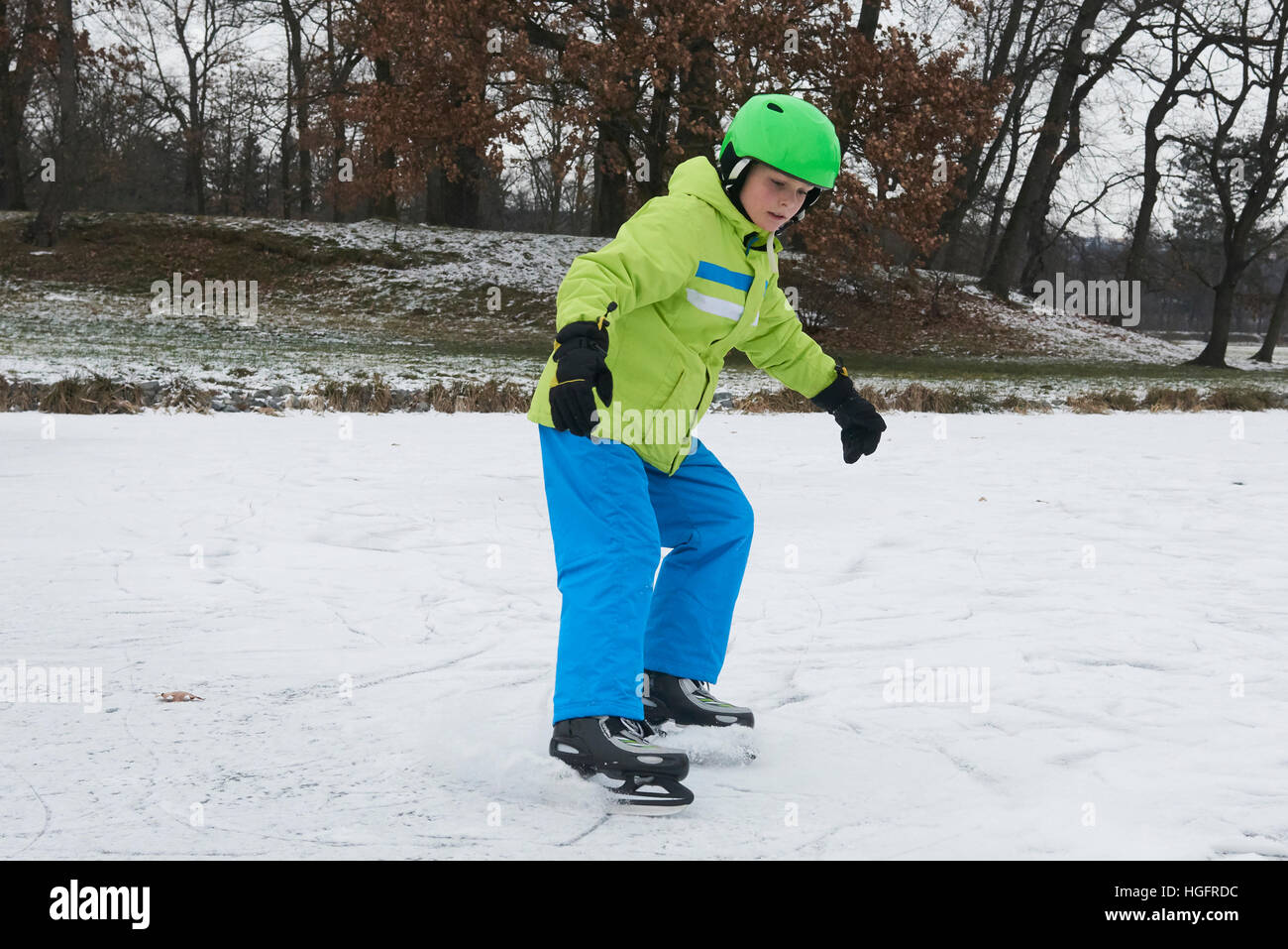 Bambino ragazzo il pattinaggio su ghiaccio in inverno la neve giorno all'aperto nel parco sul laghetto congelato. Indossando il casco di sicurezza Foto Stock