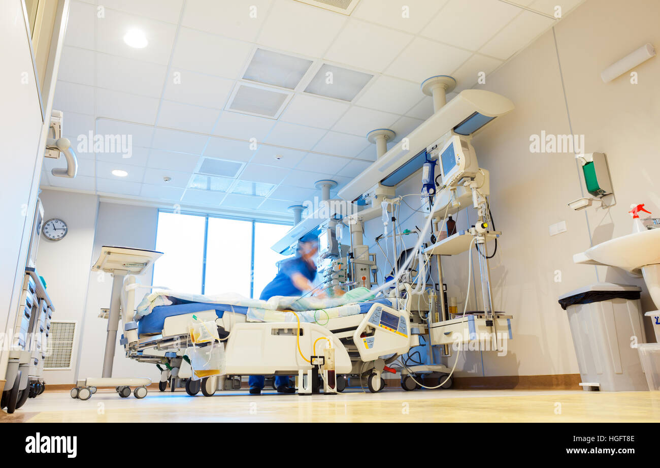 Un ospedale sala di rianimazione con moderne attrezzature mediche e sfocata paziente e infermiere o medico figure. Foto Stock