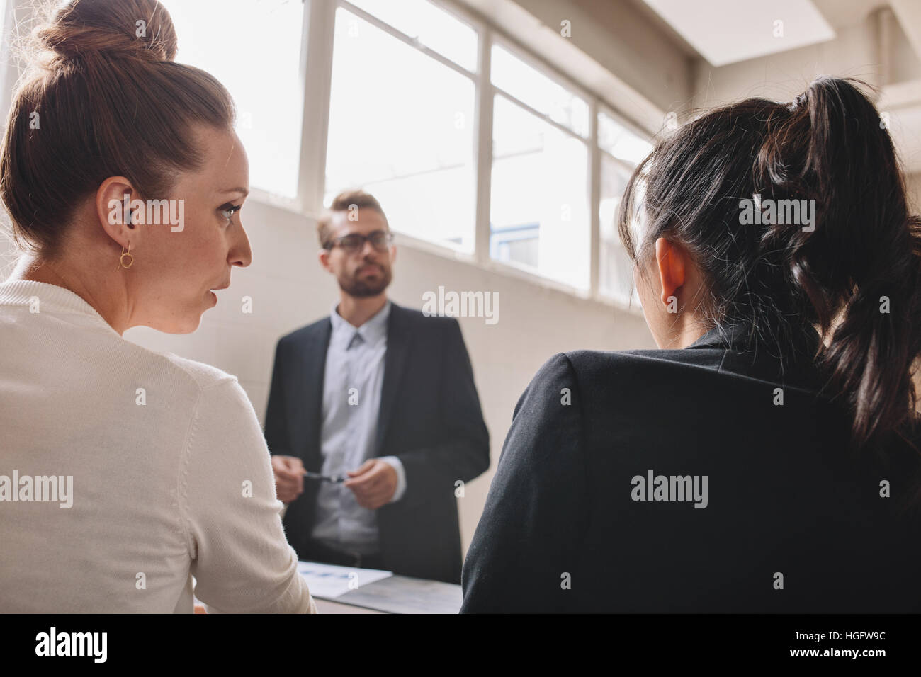 Due giovani donna discutere durante una riunione in ufficio. Imprenditore in piedi in background con le colleghe parlando davanti. Foto Stock