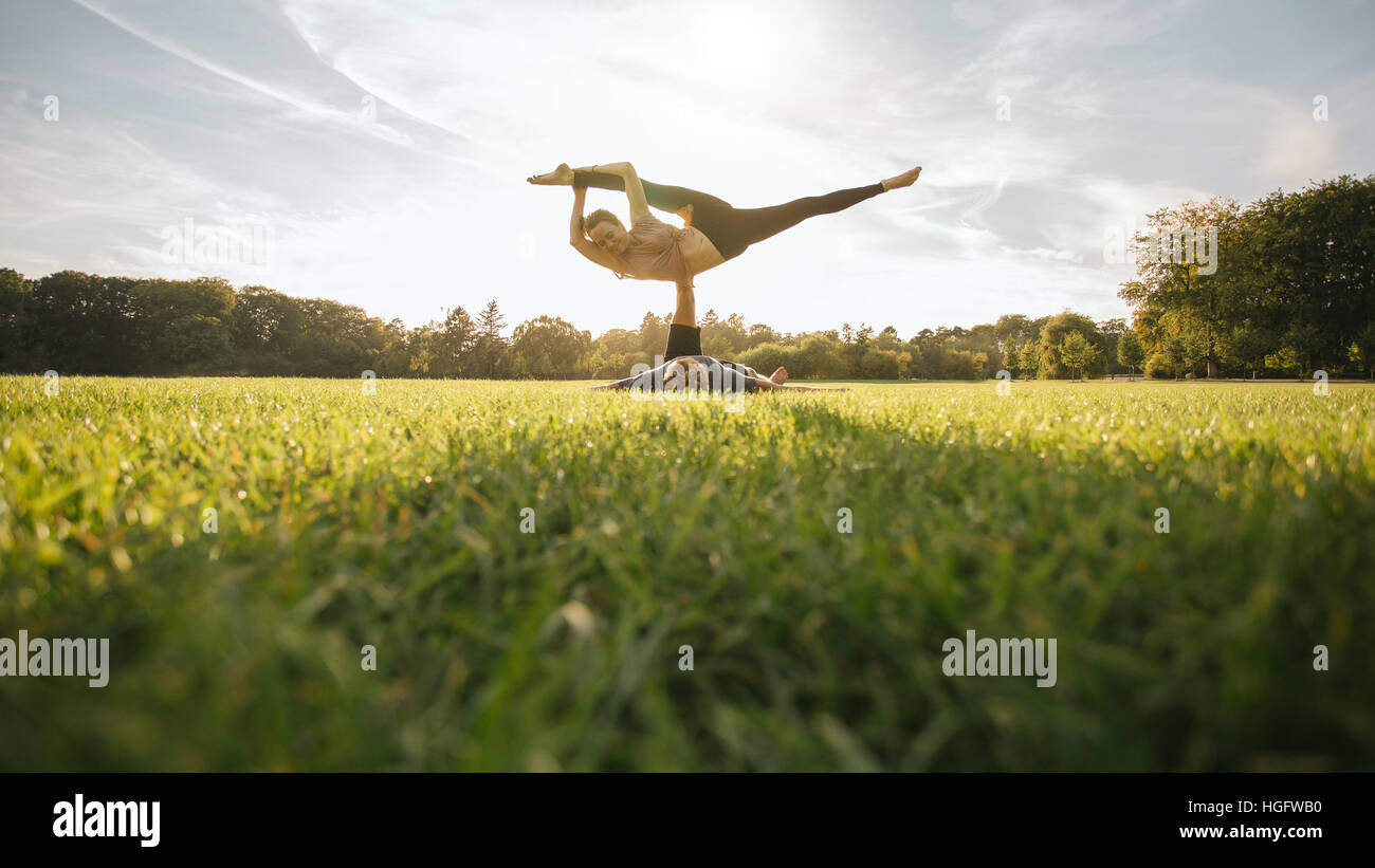 Uomo e donna coppia facendo yoga outdoor sull'erba. Montare la coppia giovane praticante acroyoga. Sollevamento di uomo e di donna di bilanciamento su una gamba al parco. Foto Stock