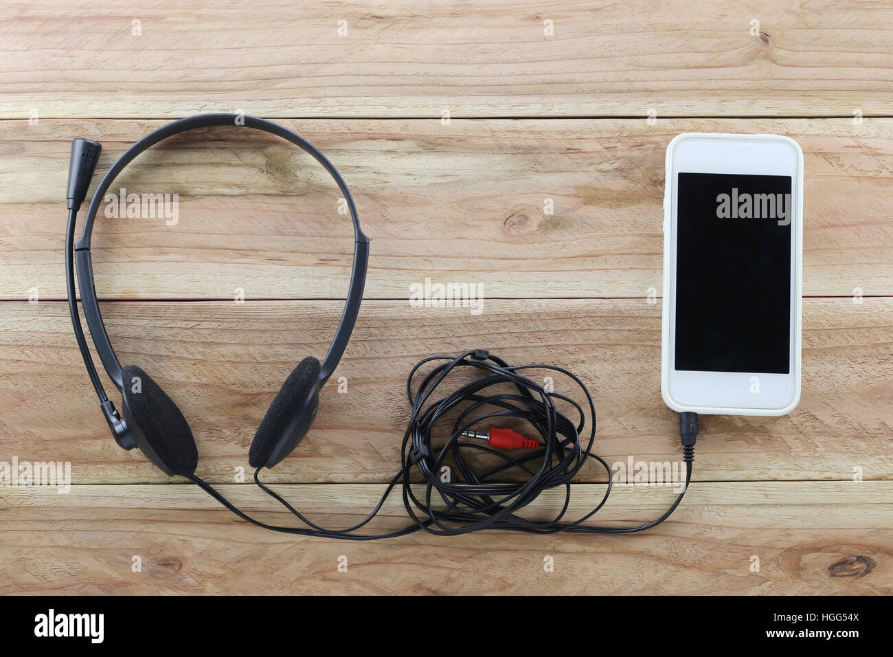 Lo smartphone bianco su marrone uno sfondo di legno e un auricolare è collegato,concetto di musica e tecnologia. Foto Stock