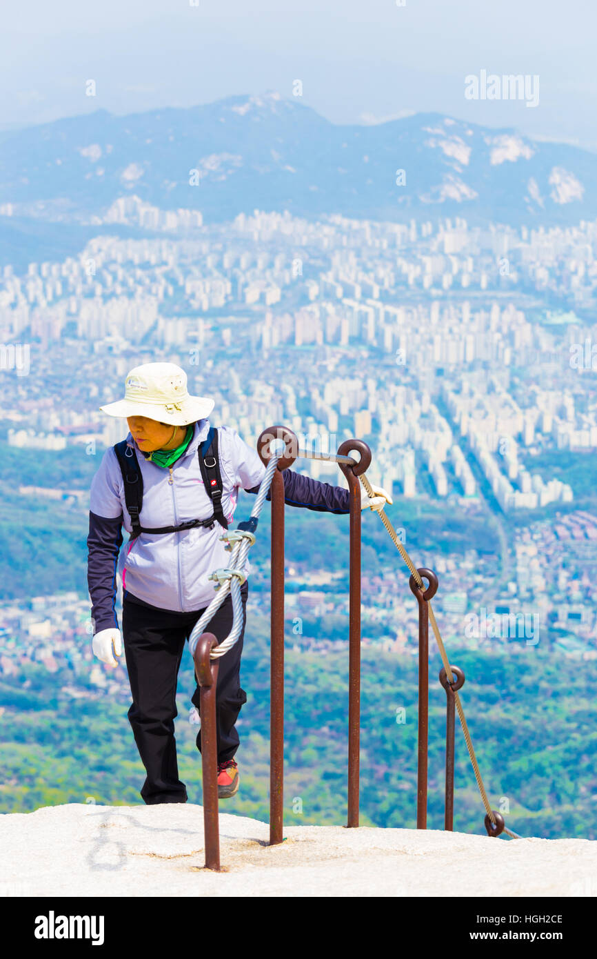Il coreano femminile pieno da indossare vestiti escursionismo avvicinando Baegundae, picco di montagna Bukhansan con vista del centro città Foto Stock