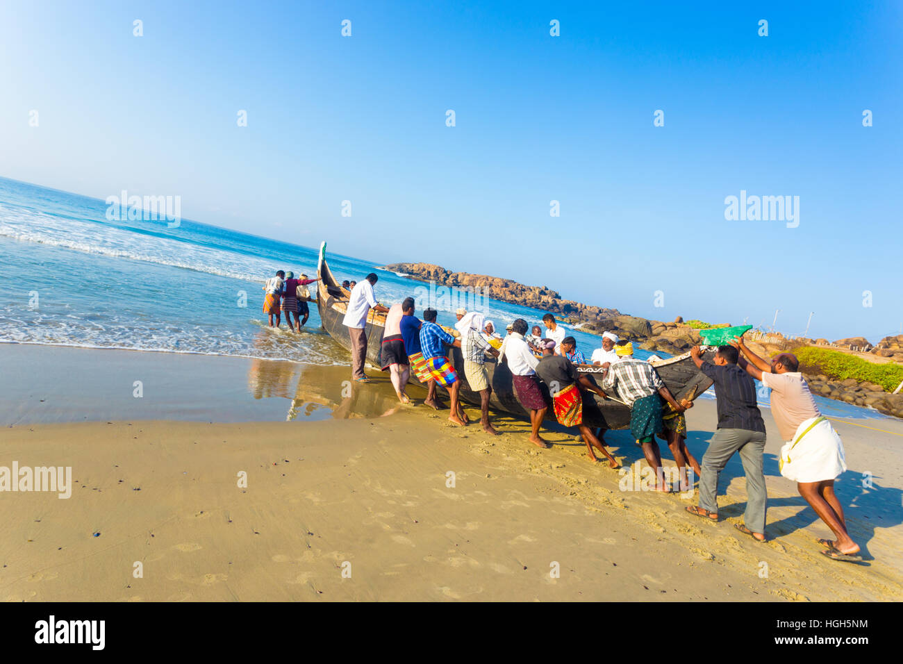 Comunità aiutando lo sforzo degli abitanti di un villaggio spingendo la pesca in barca insieme dalla spiaggia di sabbia in acqua su una mattina di sole in Kovalam, ke Foto Stock