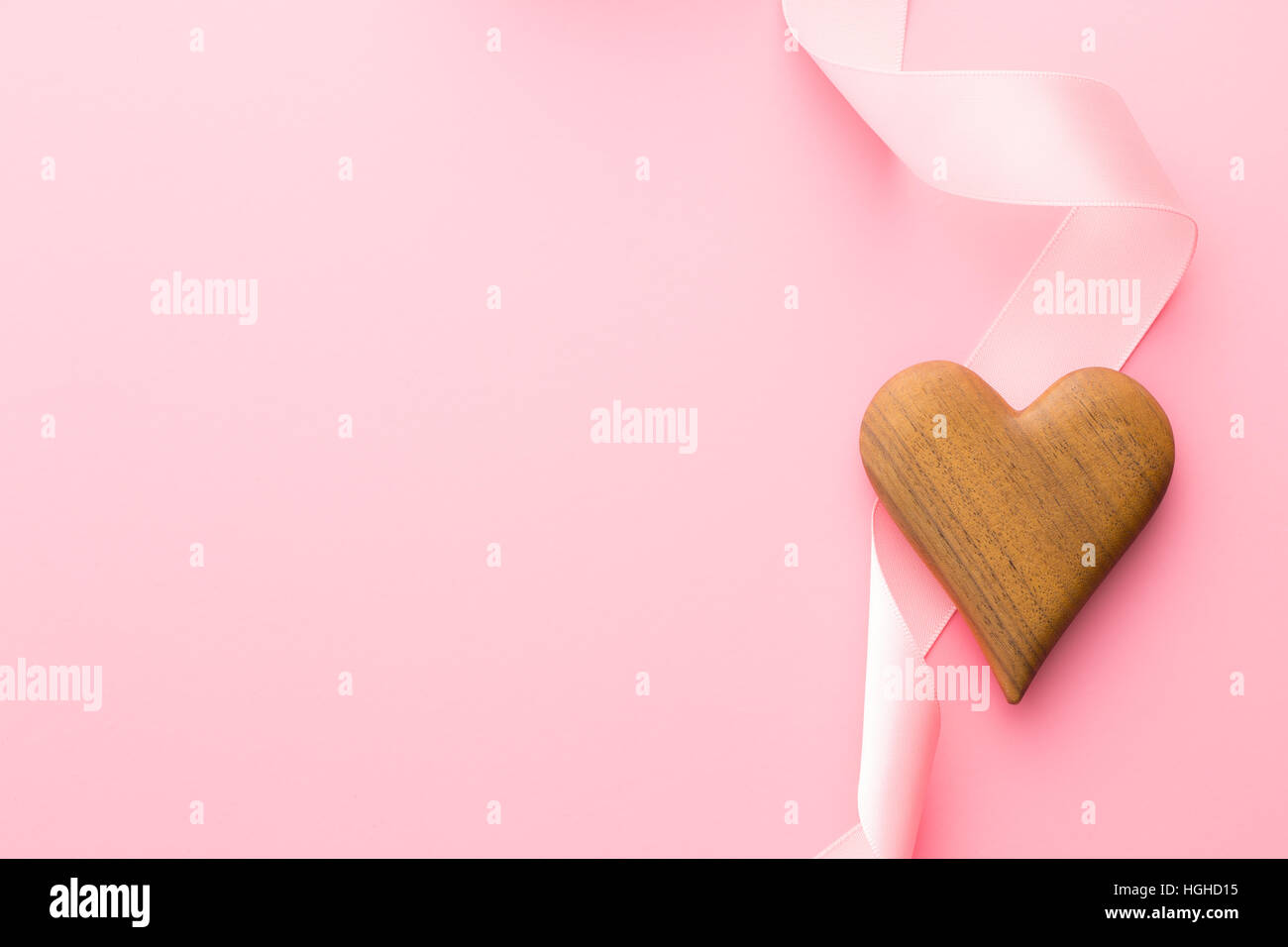 Cuore di legno e nastro rosa su sfondo rosa. Foto Stock