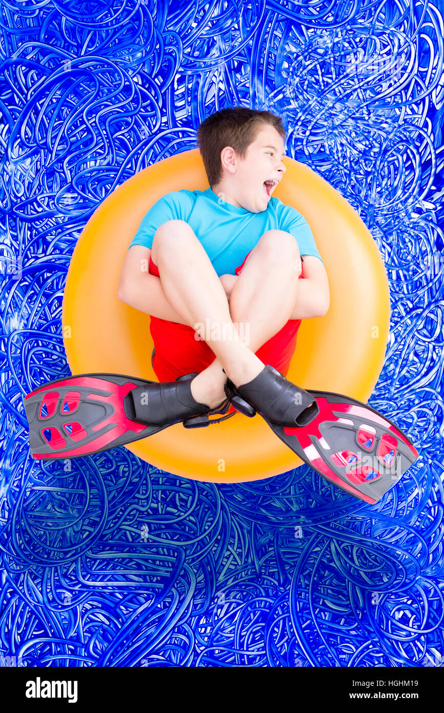 Loud noisy little boy a giocare in piscina in un caldo giorno d'estate galleggianti in un anello in plastica nel suo pinne, immagine concettuale nel blu dipinto wate Foto Stock