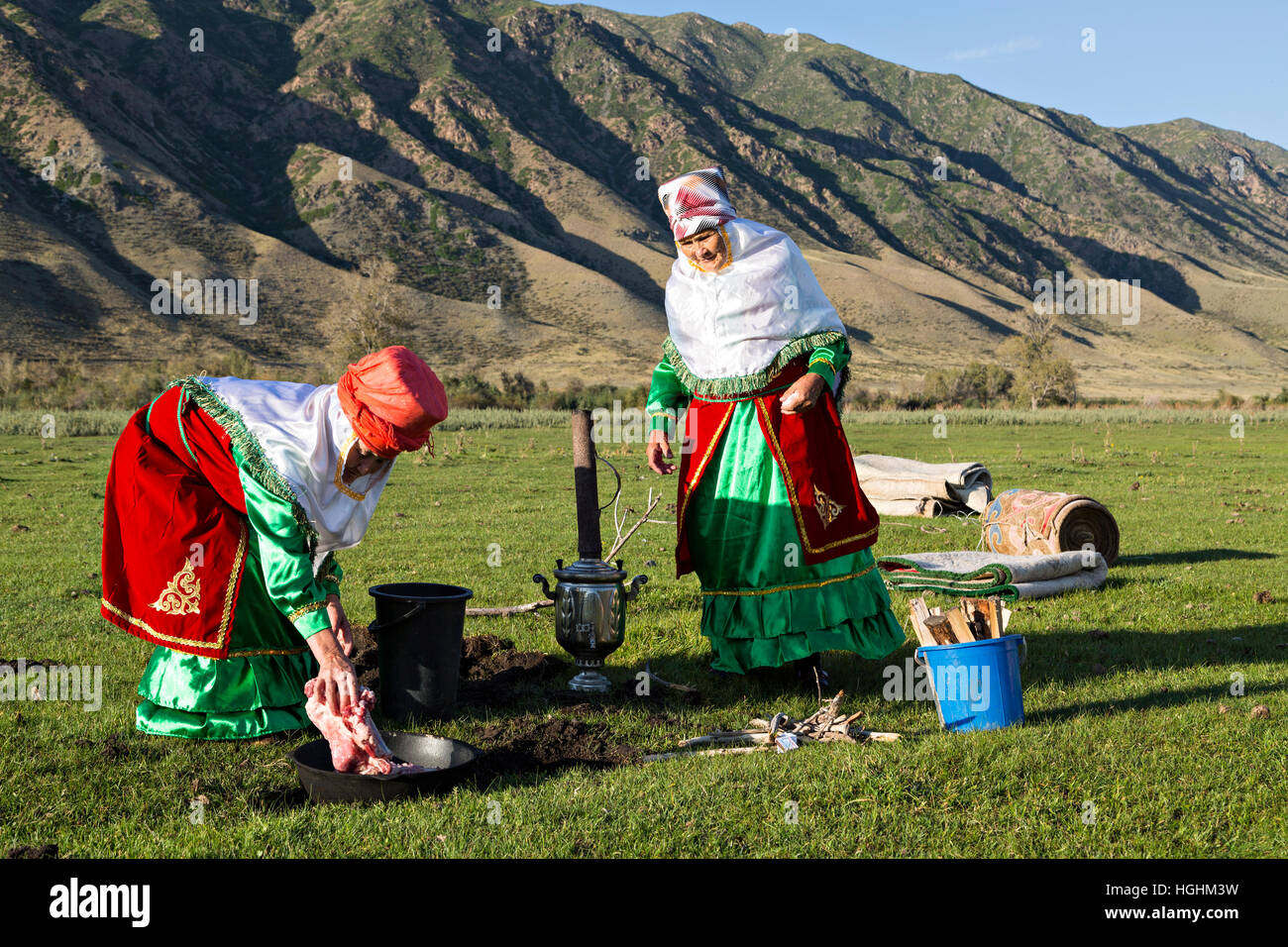 Il kazako donne in costumi nazionali cucinare la carne all'aria aperta, nel villaggio di soggiornare, Kazakistan Foto Stock