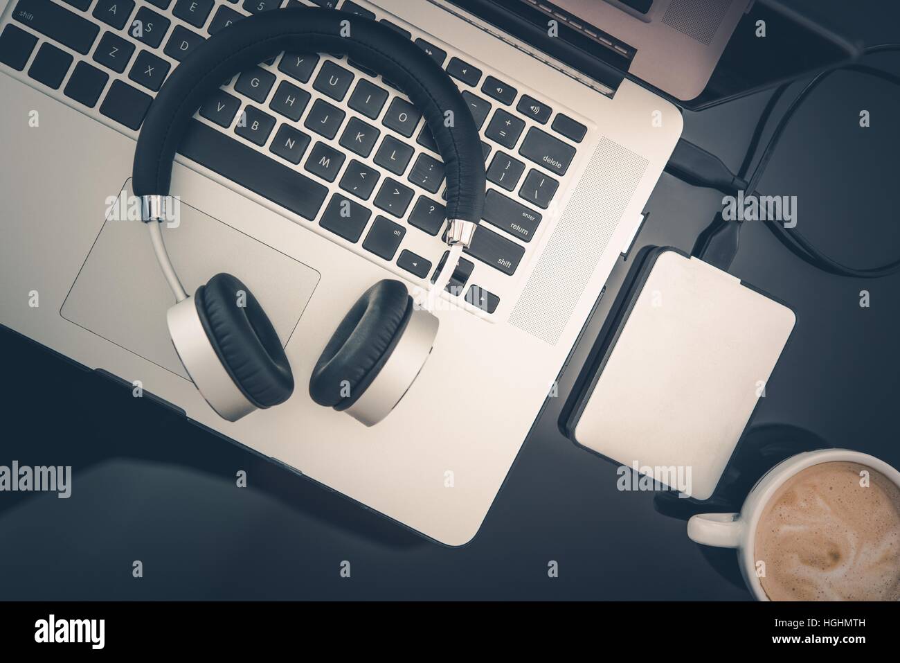 Lavoratore Freelance Mobile Workstation desktop. Computer portatili, cuffie, piccolo disco rigido portatile e la tazza di cappuccino fresco caffè sulla vetroso nero Foto Stock