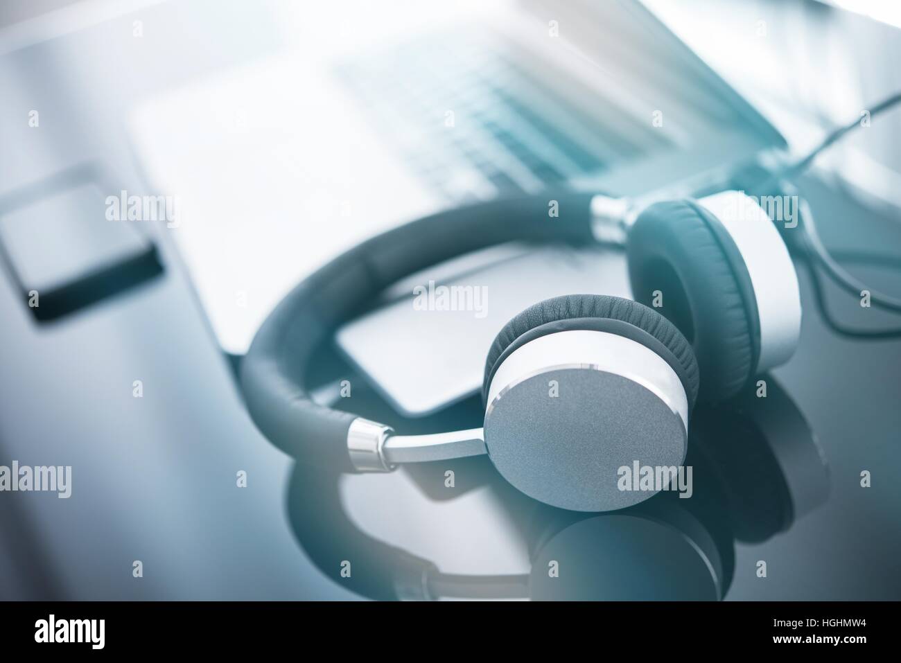Le cuffie e il computer. L'ascolto di musica online concetto foto con moderne cuffie wireless e computer laptop sulla scrivania vetroso. Foto Stock