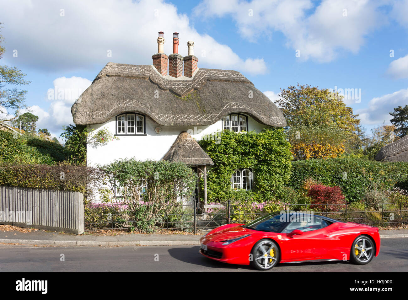 Ferrari auto sportive passando cottage con il tetto di paglia al Swan verde, Lyndhurst, Hampshire, Inghilterra, Regno Unito Foto Stock