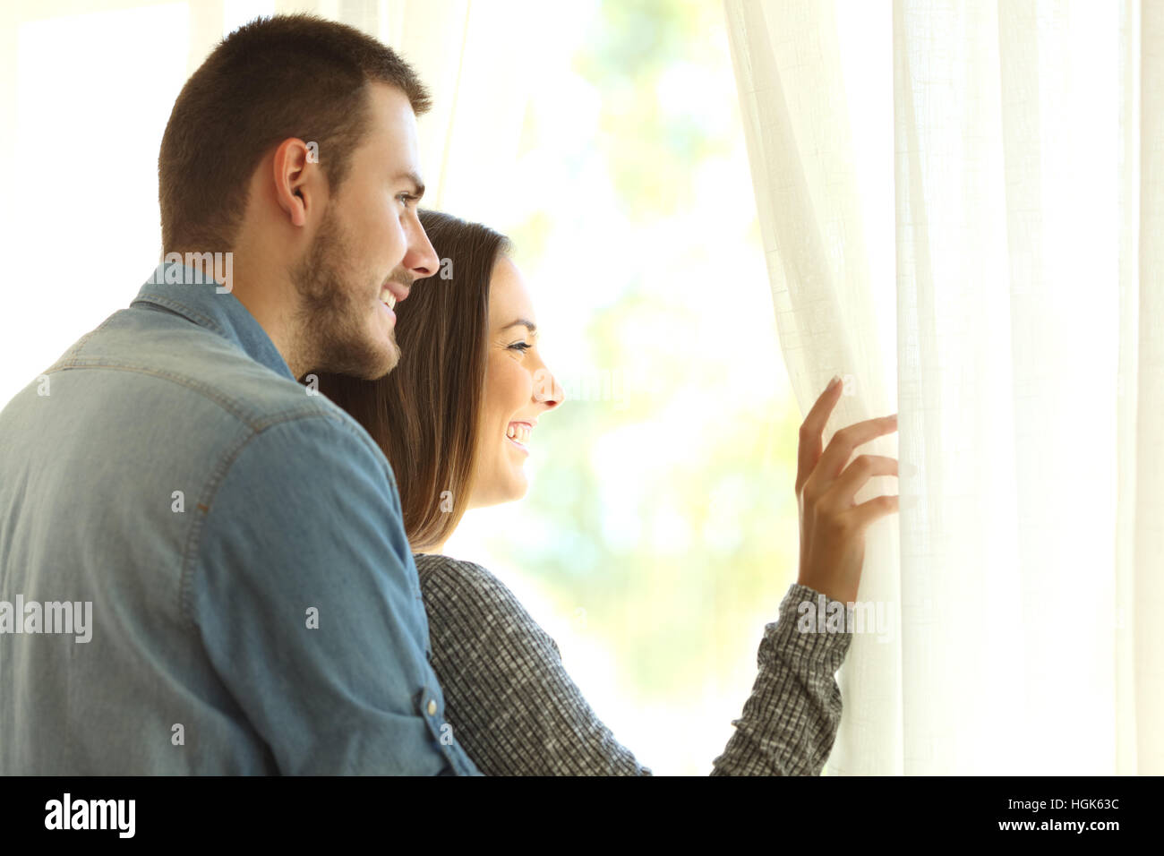 Affettuosa matrimonio aprendo le tende e guardando al di fuori attraverso una finestra in una nuova bellissima giornata con una luce calda Foto Stock