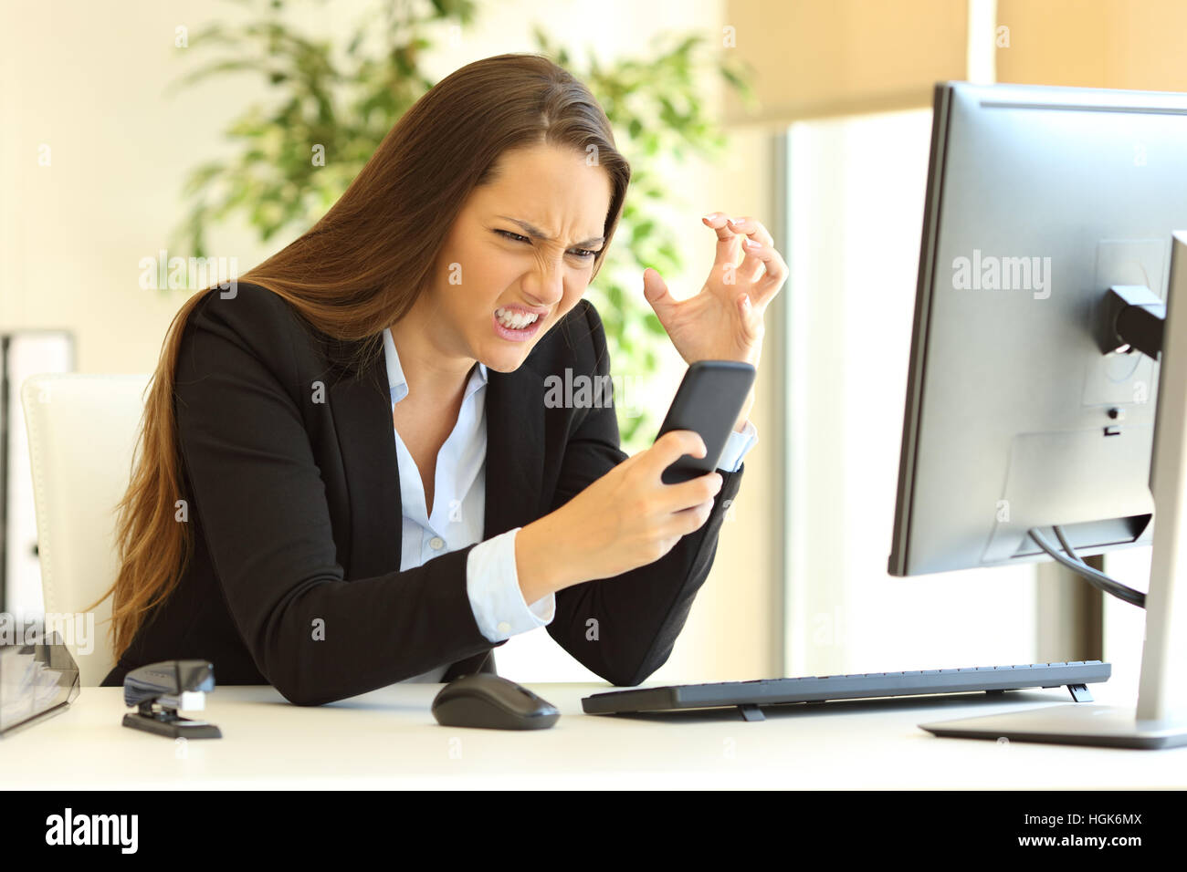 Furious imprenditrice indossare tuta lavorando sulla linea utilizzando uno smart phone in una scrivania in ufficio Foto Stock